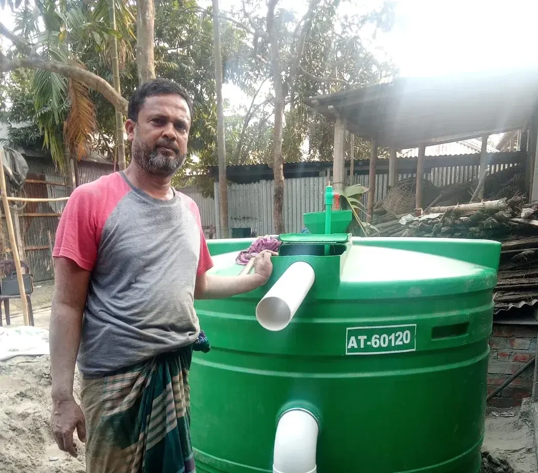A man standing beside a green household biodigester in Bogra